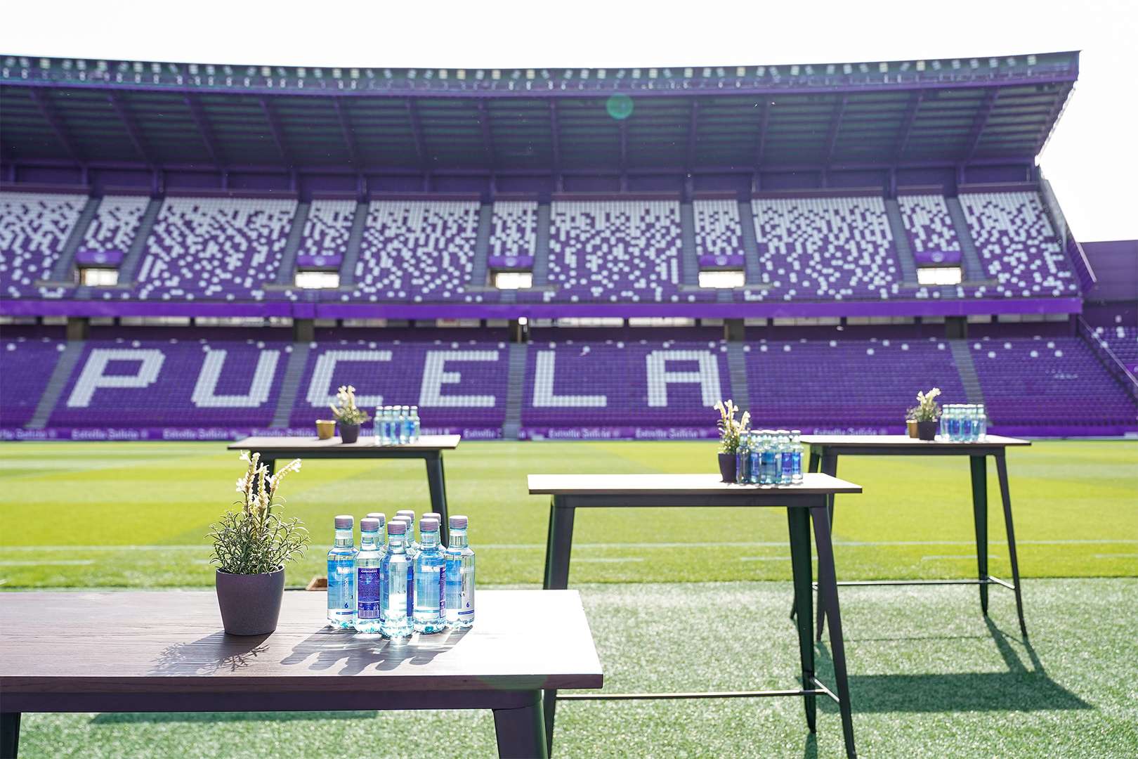 Mesas con botellas de agua en la banda del campo, con vistas al terreno de juego y a las gradas, para 100 personas