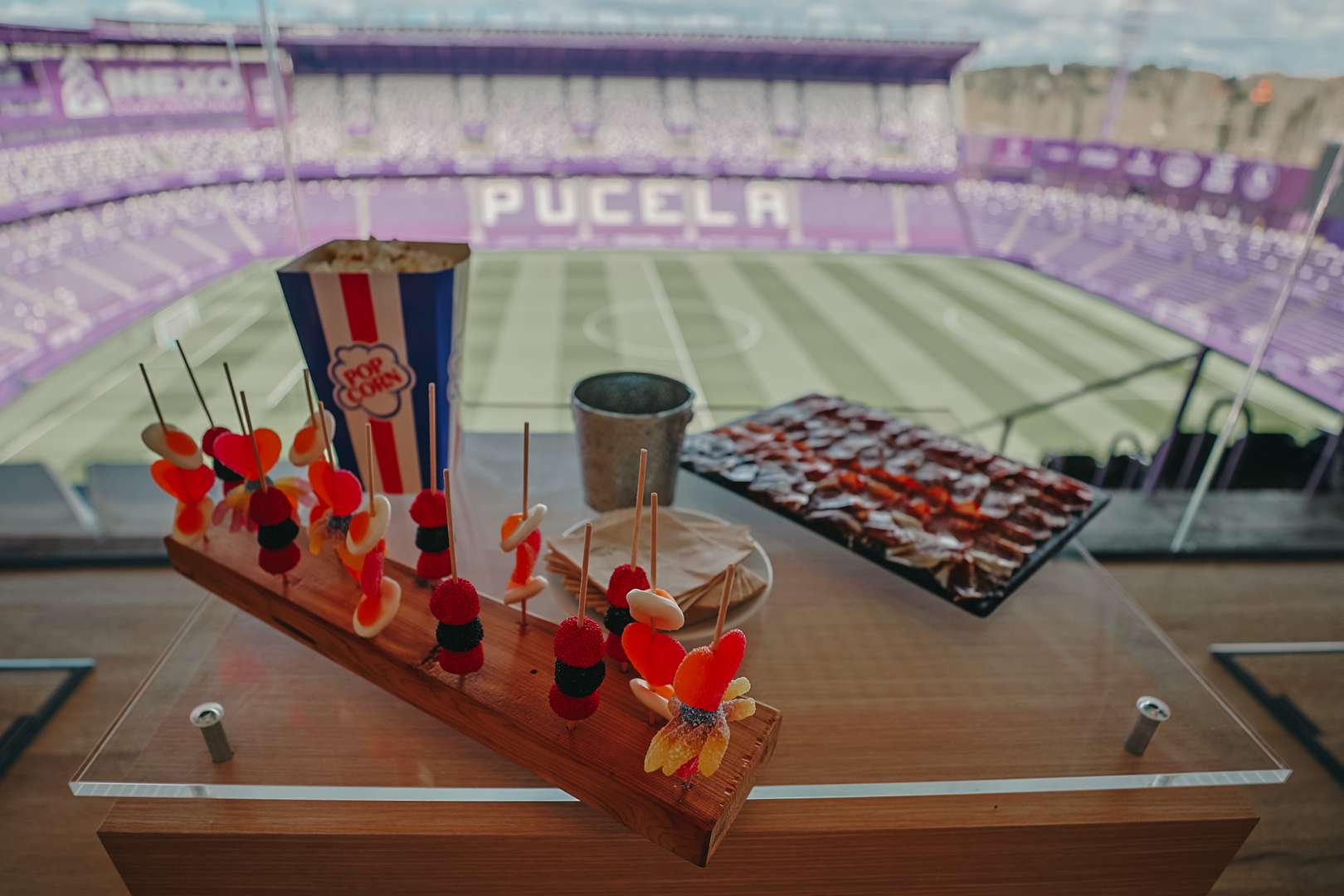 Catering con dulces, palomitas y embutidos en primer plano, con la vista del terreno de juego al fondo