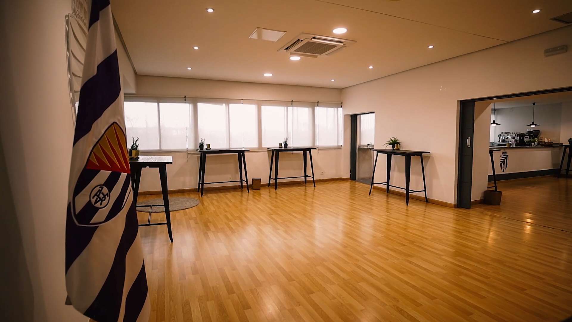 Gran sala con suelo de madera, mesas altas y la bandera del Real Valladolid