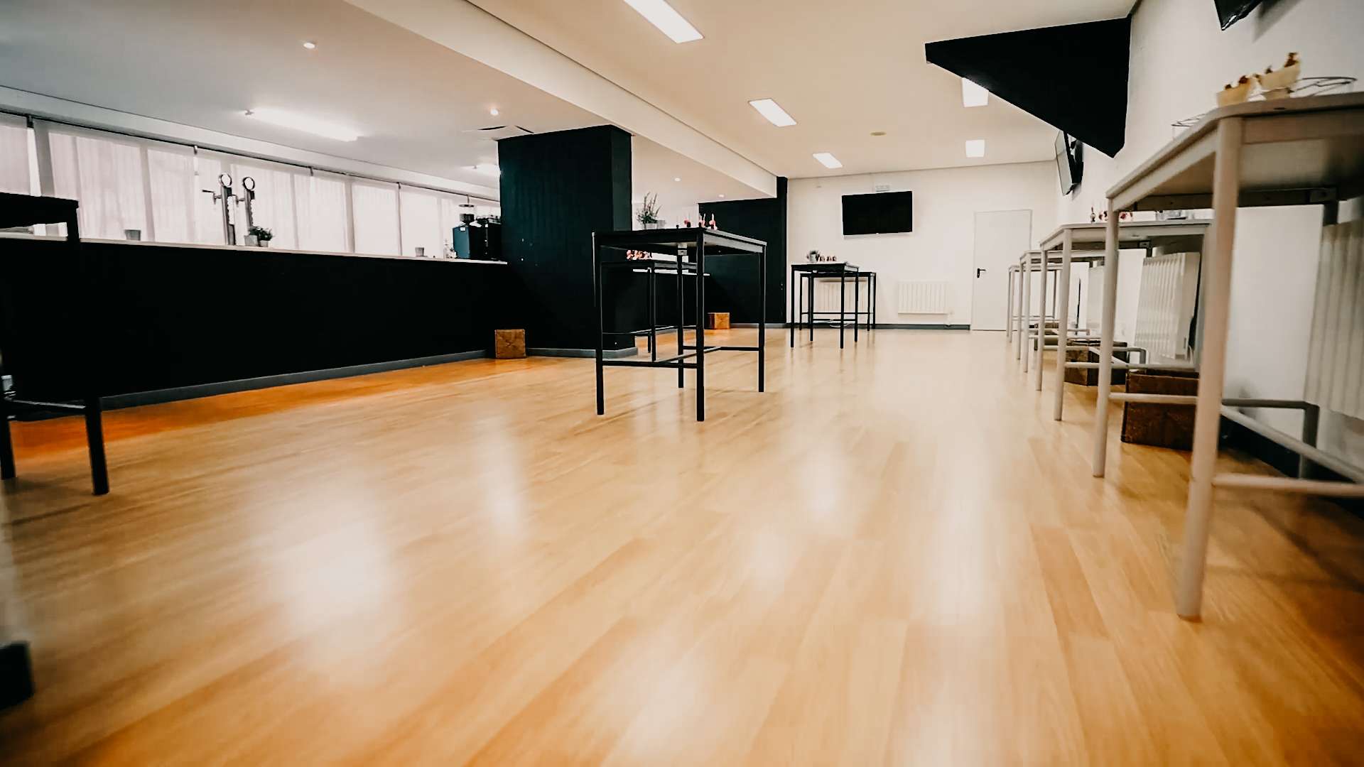 Gran sala con suelo de madera, mesas altas y una barra de bar